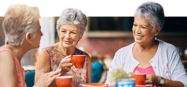 three elderly women sitting down and drinking coffee