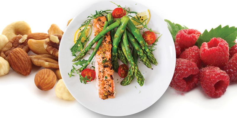 a plate of salmon and asparagus in front of raspberries and walnuts